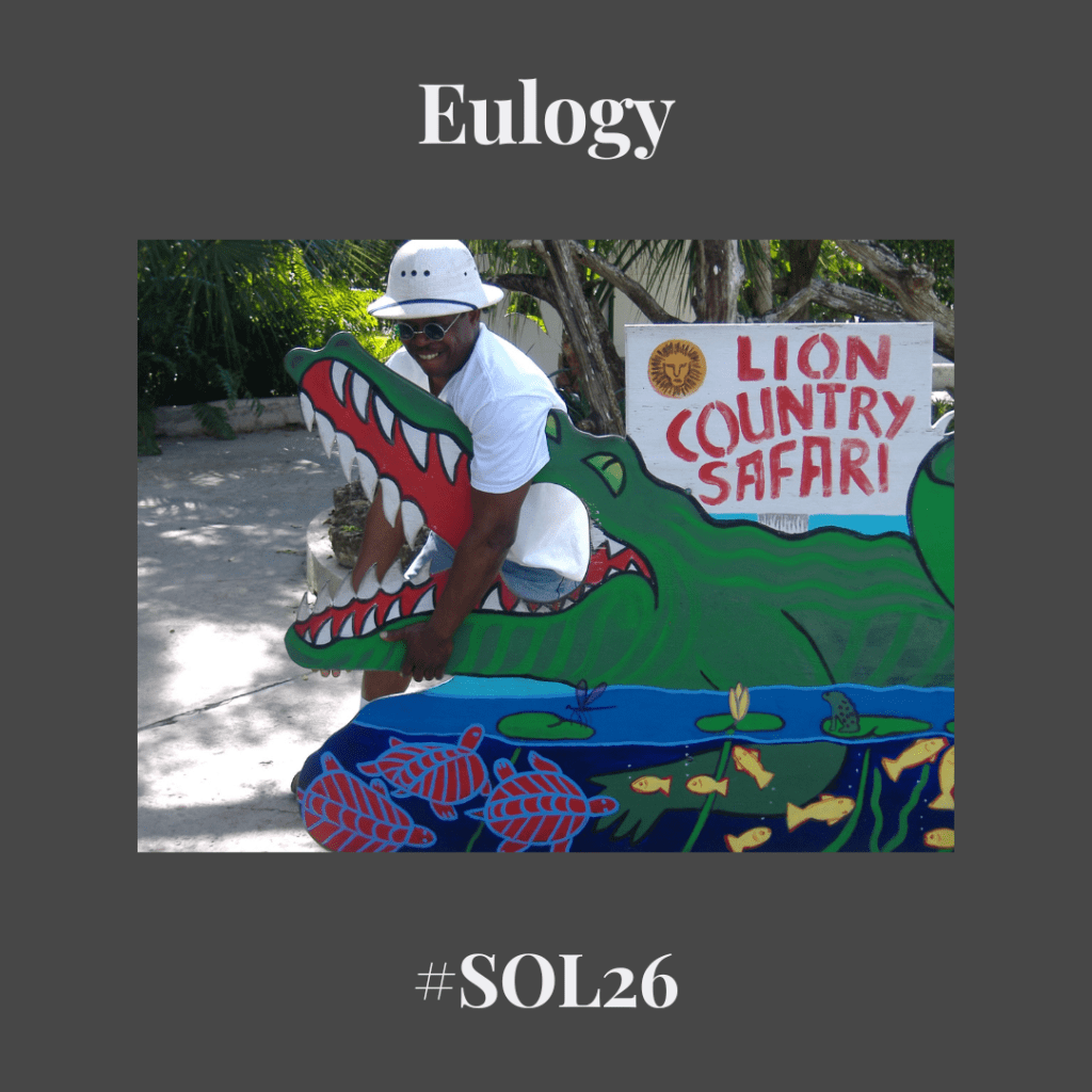 picture of a Black man in a white tee and hat wrangling the jaws of a fake alligator with a Lion Country Safari sign in the background