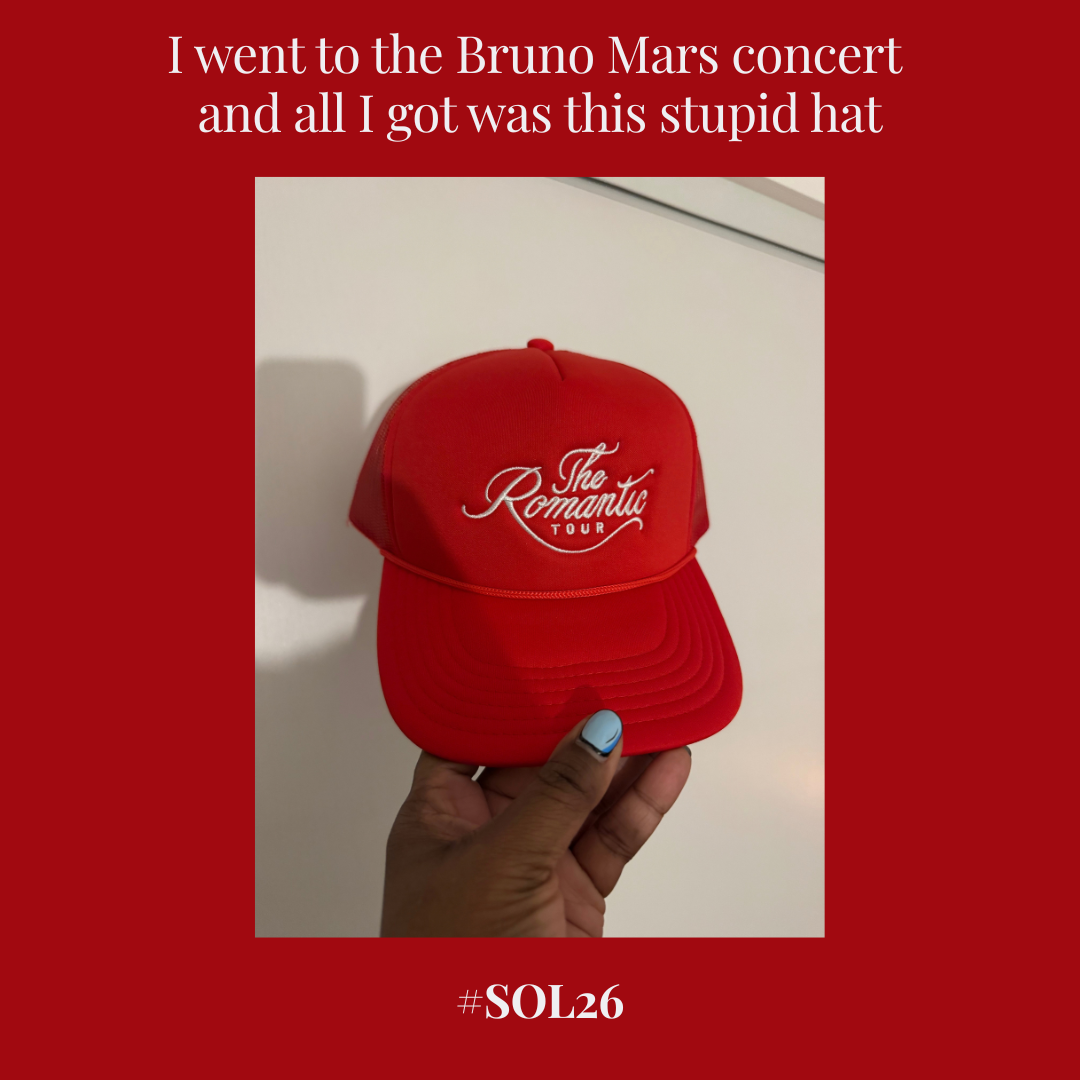 Cinder An image set against a deep red background with white serif text at the top reading "I went to the Bruno Mars concert and all I got was this stupid hat". In the center, a hand with light-blue painted fingernails holds up a bright red trucker-style hat featuring white embroidered cursive text that reads "The Romantic TOUR". At the bottom center of the red frame, the hashtag "#SOL26" is printed in white serif font.